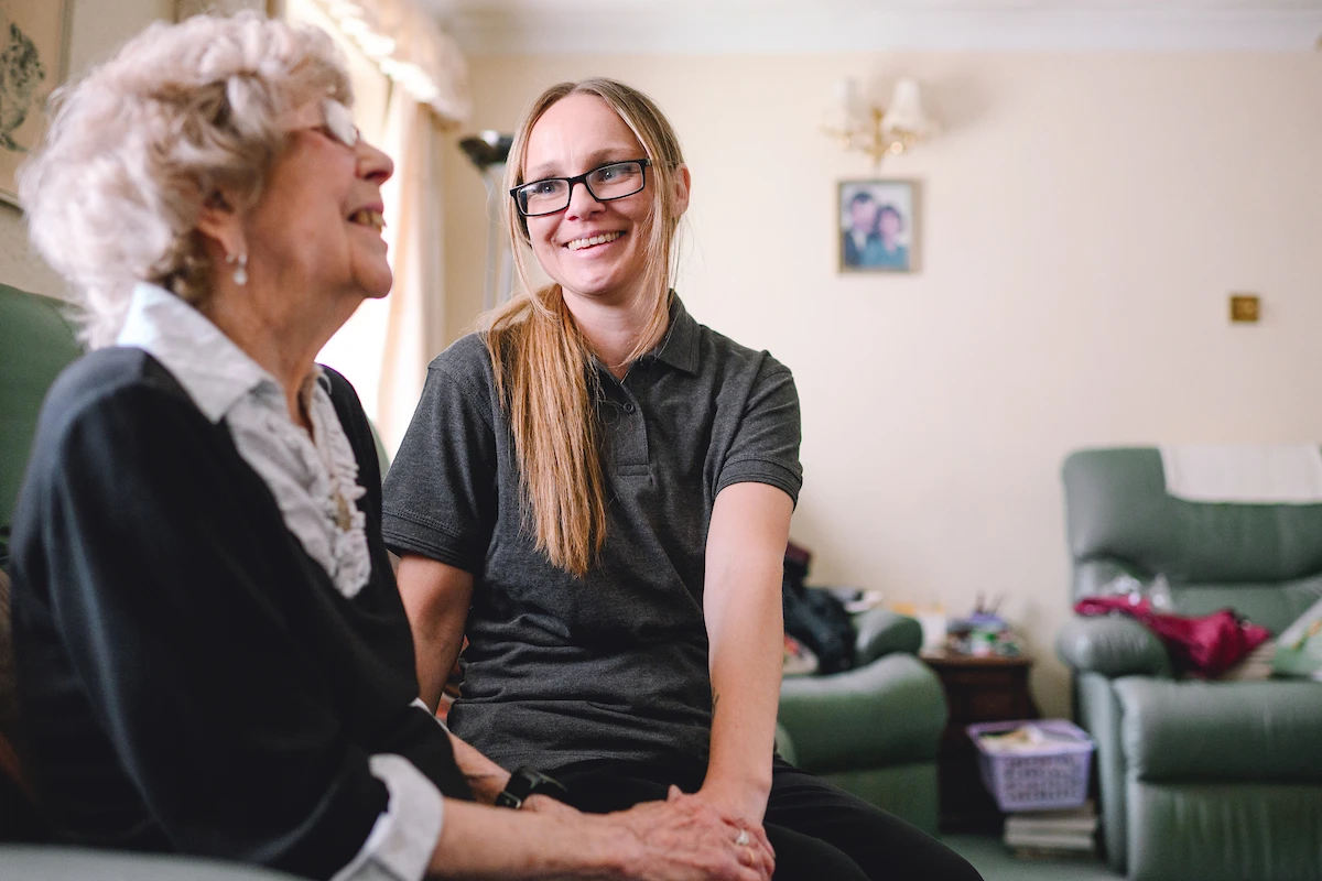 Nestwell home care assistant sitting and chatting with an elderly woman in her living room.