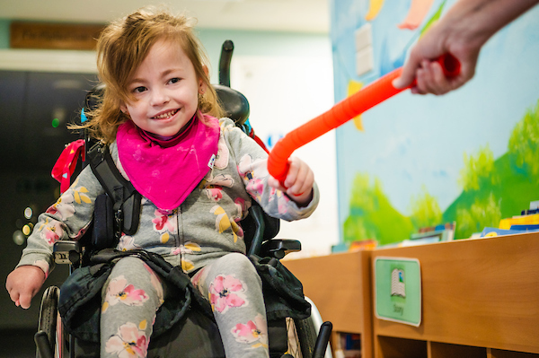 Smiling young child in a wheelchair playing with a carer during a support session at Chestnut Tree House.