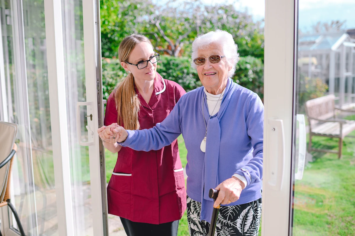 Home care assistant helping an elderly woman into her house from her garden.